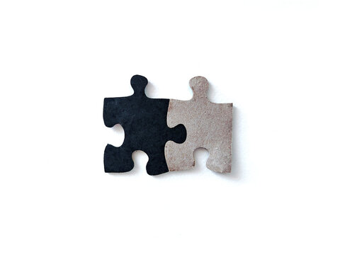 Two interlocking black and beige jigsaw puzzle pieces on a white background, representing teamwork, connection, cooperation, problem solving, and business collaboration.