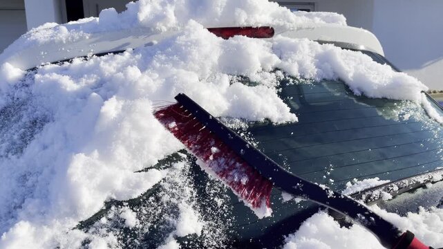 Cleaning car back windscreen from snow with the brush tool, sunny winter day