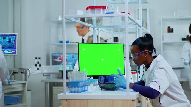 Typing, chroma and scientist workflow as a woman uses a computer with a blank green display beside test tube racks and a microscope, for scientific software mockups and digital laboratory content.