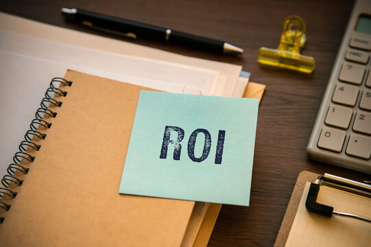 ROI sticky note reminder on workspace notebook &mdash; ideal for finance blog posts and investment strategy articles