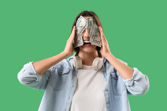 Greed and materialism concept, young woman covering eyes with hundred dollar bills, financial success and obsession with money on green background