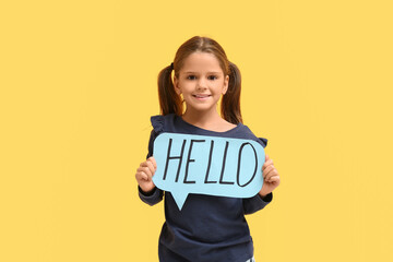 Cute little happy girl holding paper speech bubble with word HELLO on yellow background © Pixel-Shot