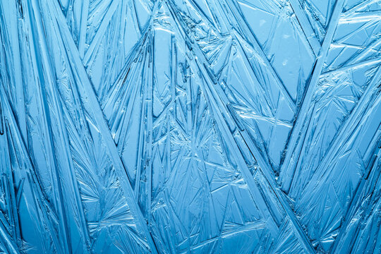 Ice frozen in intricate patterns of delicate crystals in blue and teal. Detailed textures of real unique patterned crystal formations. Sparkling window frost or icy cold winter frosting background.