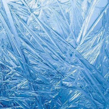 Ice frozen in intricate patterns of delicate crystals in sparkling blues. Detailed textures of real unique patterned crystal formations. Sparkling blue window frost or cold winter frosting background