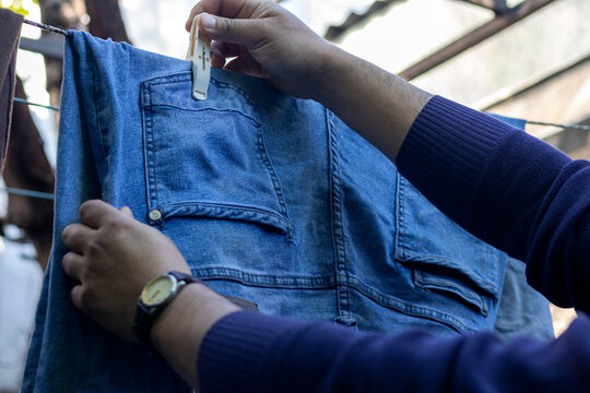 Horizontal stock photo of hands securing blue denim jeans with a white clothespin on a clothesline