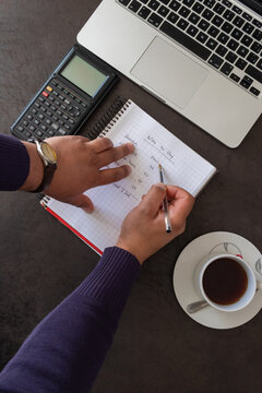 Top view of person writing household budget in finance notebook with laptop and coffee