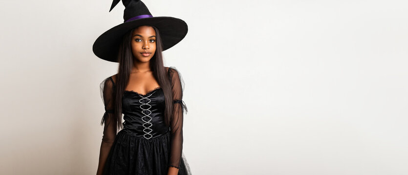 young black teenage girl wearing a black witch hat and dress looking at camera on a plain background