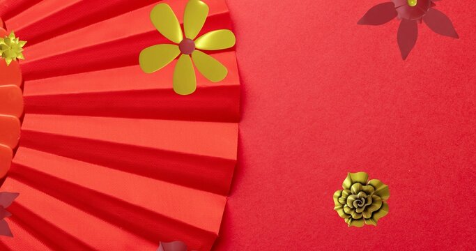 Displaying pleated red paper fan on studio flat-lay, with gold flower, maroon cutouts, copy space