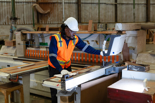 Wood workshop: woodworking with plywood, a carpenter reads documents while touching the control panel of a nearby panel saw.