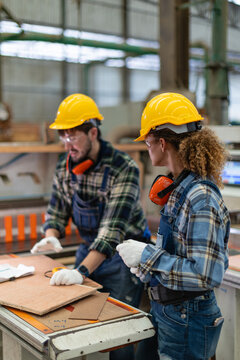Female carpenter: woman in a carpentry workshop examines wood with her male colleague holding a tape measure beside the table saw.