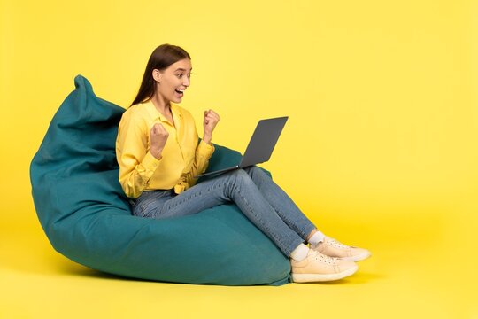 Excited Young Woman With Light Skin And Straight Hair Celebrating Success With Fists Raised While Using Laptop At Home. Focused On Achievement In A Relaxing Environment. Weight Loss Concept.