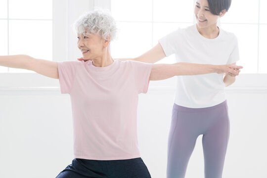 インストラクターにヨガポーズを教わるシニア女性　健康イメージ