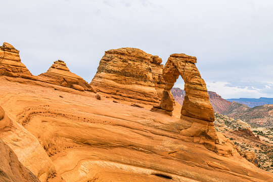 The iconic Delicate Arch standing gracefully on a sweeping sandstone bowl formation under a cloudy sky in Arches National Park, Utah.