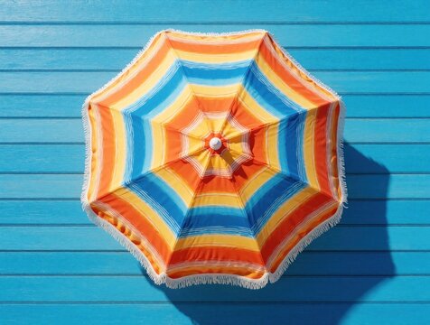 Top view of colorful striped beach umbrella on blue wooden background. Bright parasol with orange yellow, blue colors provides shade. Summer vacation concept with tropical sun protection on sea shore