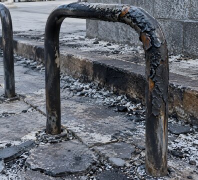 Heat blackened tubular steel bicycle stand with blistered coating standing on spalled stone flags at civic square edge