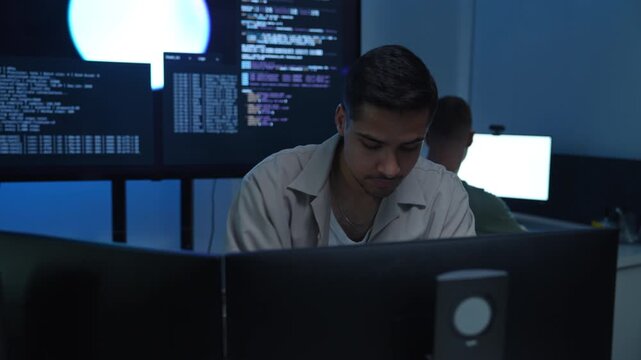 Focused AI developer and technology professional working at computer workstation in modern office, coding software and analyzing data for artificial intelligence project