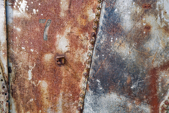 The abstract textures of rusty metal plates bolted together with the stenciled number seven