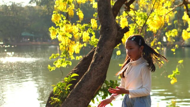 Young Girl Playing by Lake Under Blooming Golden Shower Tree