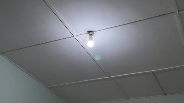 Low angle shot of a ceiling light bulb glowing steadily and flickering briefly once near the video end.   