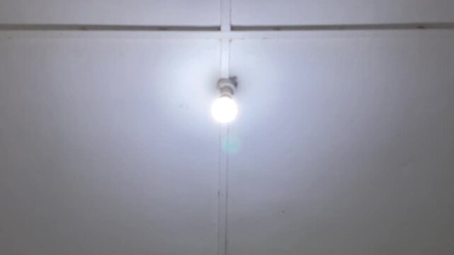 Low angle shot of a light bulb flickering continuously on the ceiling of an indoor room.