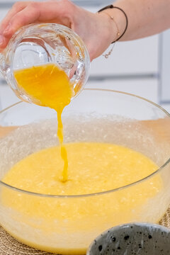 Cooking dessert. Dough preparation. Woman chef hand pouring orange juice liquid in bowl with yellow butter making flavoring fruit treat.
