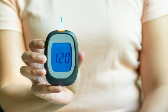 Woman holding a blood glucose meter showing a reading of 120 mg/dL, representing diabetes testing, health monitoring, medical checks, and healthcare management.concept medical