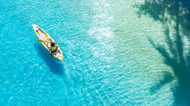 Aerial view of woman kayaking on crystal clear turquoise sea water, representing tropical travel, water sports, outdoor adventures, and relaxing vacations. concept traval