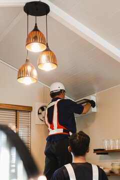 HVAC technician servicing an indoor electric box unit with coworker.