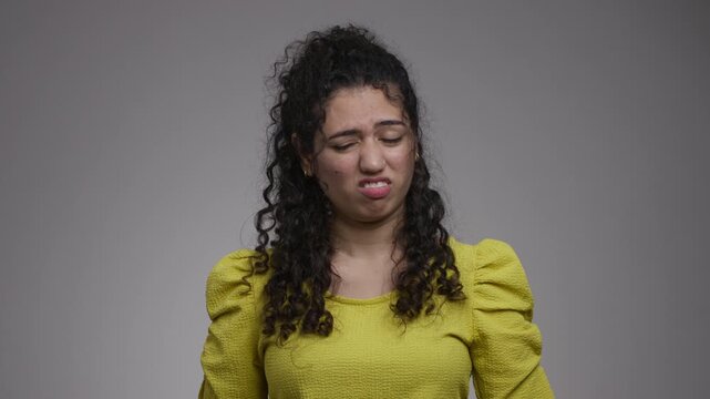 A woman furrows her brows, closes her eyes and scrunches her mouth in a displeased grimace before softening her expression.
