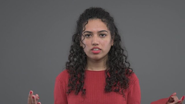 Woman in a red sweater closes her eyes, lifts her chin and raises both hands with palms upward in an exasperated gesture.