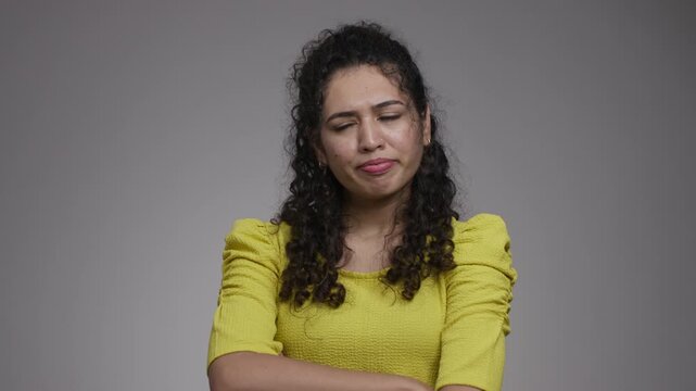 Woman in a yellow top lifts an index finger with a stern expression, then lowers her hand and looks aside with pursed lips.