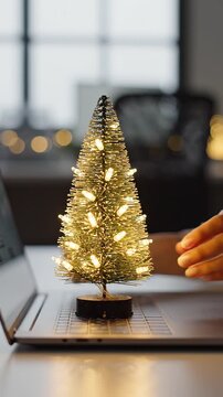 Office worker placing a mini illuminated Christmas tree on a laptop desk