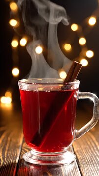 Close-up of hot mulled wine in a glass mug with rising steam and Christmas lights background