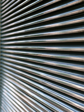 Metal grille texture with repeating horizontal rib, reflective surface, and dramatic shadow