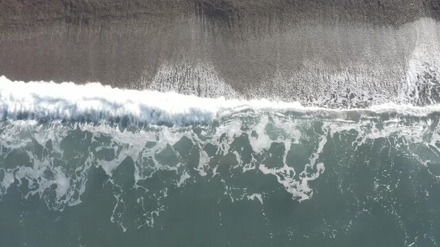 Top down aerial view of ocean waves breaking with white foam on the shore, drone footage of the Atlantic coast in Patagonia