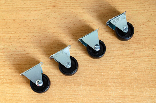 Four metal caster wheels arranged on a wooden surface with visible shadows