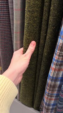 Vertical orientation slow motion close up shot of a person hand choosing olive green tweed and plaid wool fabrics in a textile shop