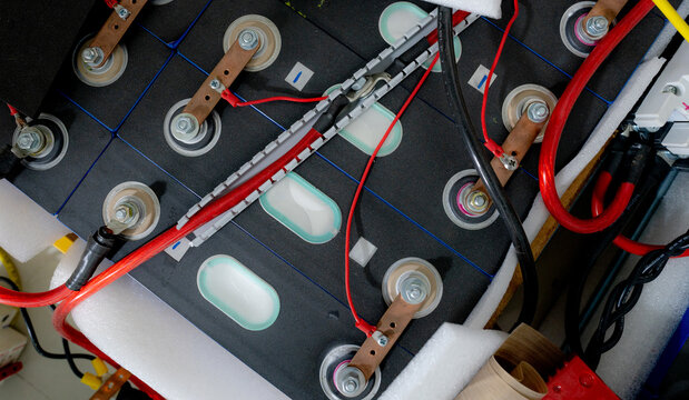 Close up of lithium ion NMC battery cells connected with copper busbars and electrical cables inside an EV battery pack, showing high voltage energy storage technology for electric transportation.