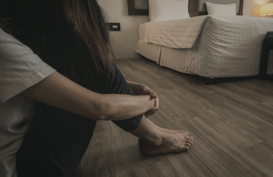 Woman sitting alone on bedroom floor beside a hotel bed with head lowered and knees held close, expressing sadness, stress and loneliness during a difficult moment, emotional wellbeing concept