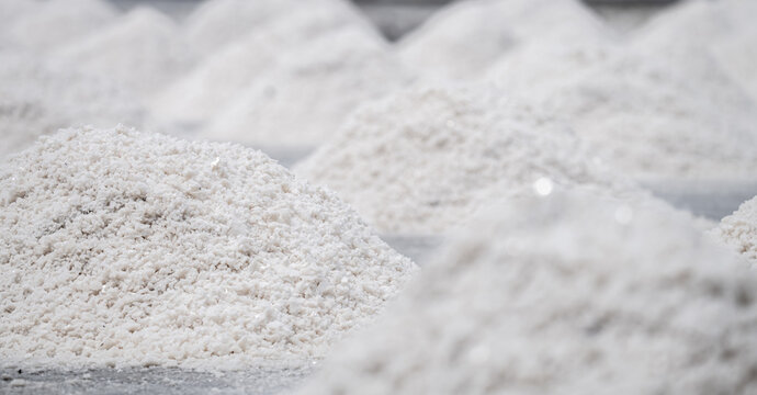 Natural sea salt crystals gathered into white piles on an evaporation field during daytime, where seawater is dried and harvested at a traditional coastal farm for food and mineral production