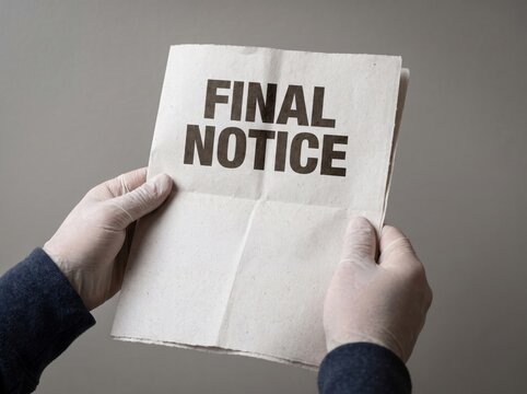 Caucasian adult wearing protective gloves holding a final notice document against a gray wall