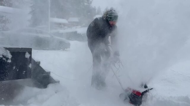 man clearing snow near wooden house in countryside using electric snow blower