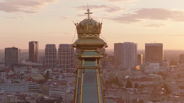 Close aerial view of the golden crown and cross atop St Martins Cathedral, set against Bratislava modern skyline and warm sunset colors in Slovakia.