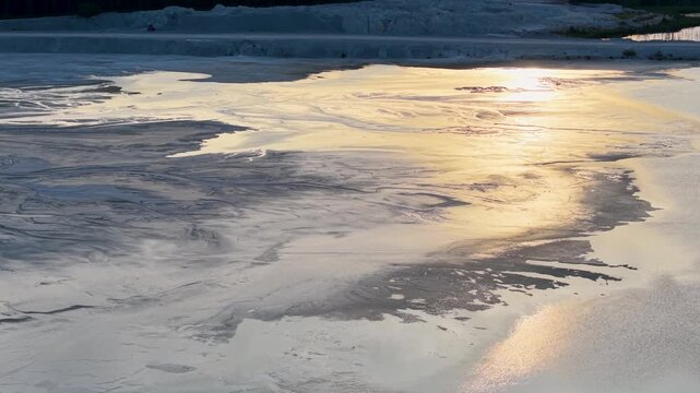 Low aerial view captures golden sunlight reflecting across shallow water and rippled sediment along a broad Lake Huron mudflat