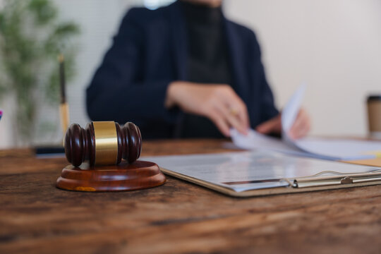 Justice in Session: A judge's gavel rests on a wooden desk, with hands blurred in the background shuffling legal documents, symbolizing the intricate process of law and order.