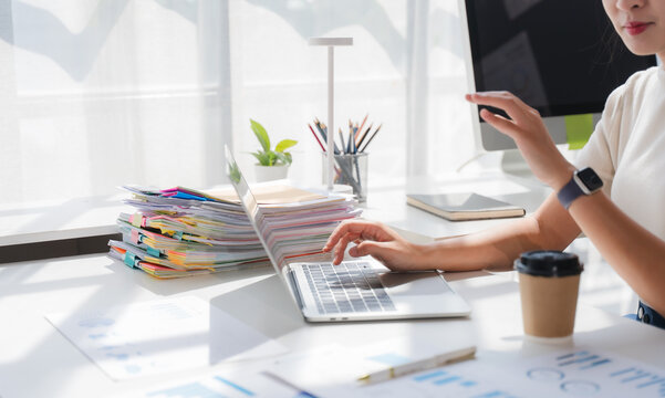 Focused at Desk: A focused professional works diligently on a laptop in a bright, modern office, surrounded by stacks of documents and a hot beverage, embodying productivity and modern work culture.