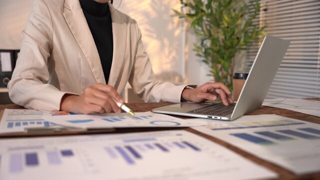 Financial Analysis Session: A professional meticulously analyzes financial charts and graphs on her laptop, surrounded by important documents and reports.