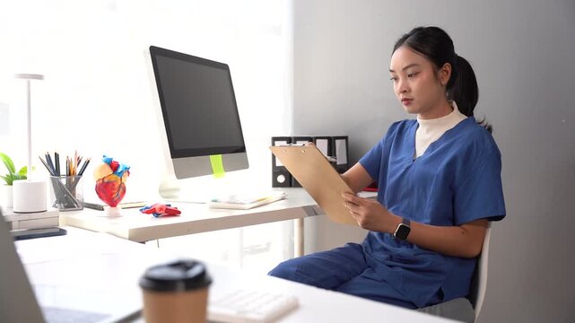 Medical Professional at Desk: A focused female medical practitioner in blue scrubs reviews a document at her desk, with a computer, anatomical model, and coffee cup nearby.