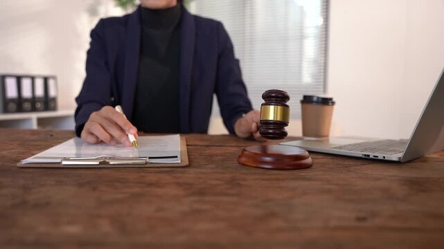 Legal Professional at Work: A focused legal professional, dressed in formal attire, sits at a wooden desk, meticulously reviewing documents with a gavel and laptop nearby.