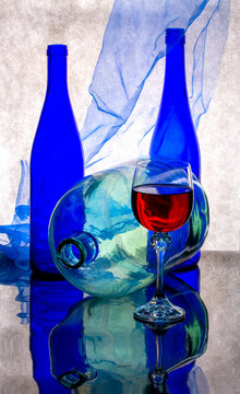 Still life with a blue and red bottle, a glass of wine and a glass jar